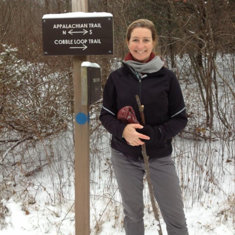 woman standing next to a trailhead sign smiling